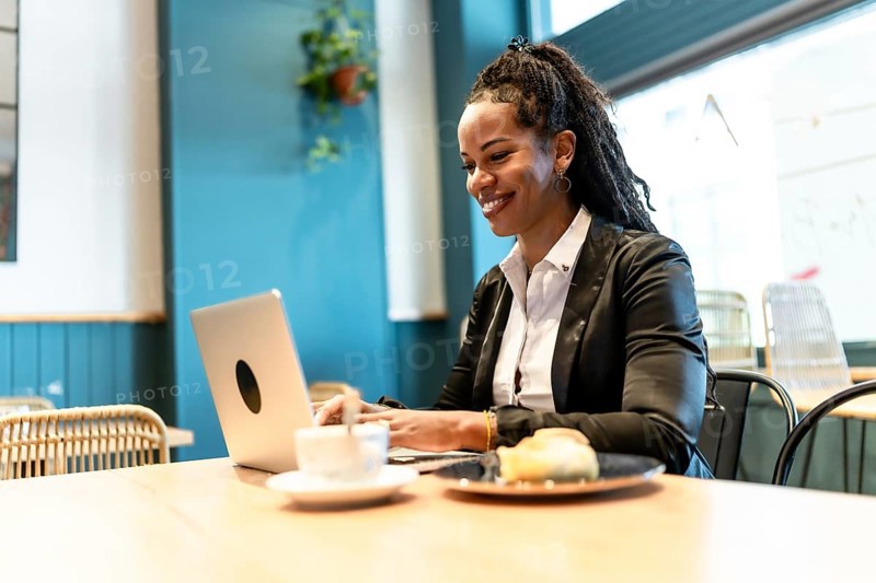 Confident latin businesswoman working with laptop in a cafeteria while eating sandwich and drinking coffee