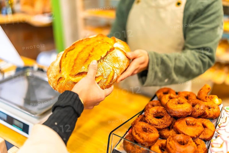 Close-up of the hands of a salesman handing a round artisan bread to a female customer