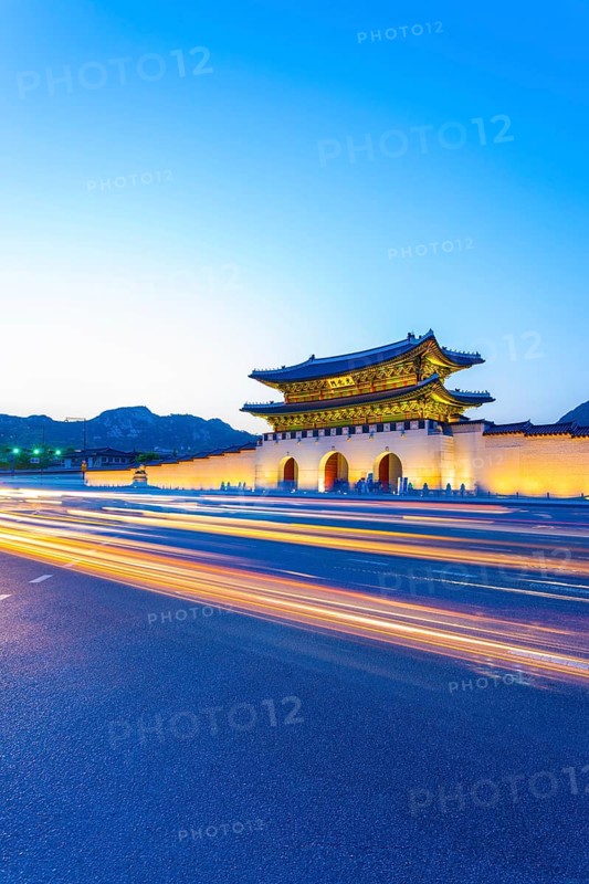 Colorful streaking car lights passing in front of lighted gate of Gwanghuamun, entrance to historic Gyeongbokgung Palace at twilight in downtown Seoul, South Korea. Vertical