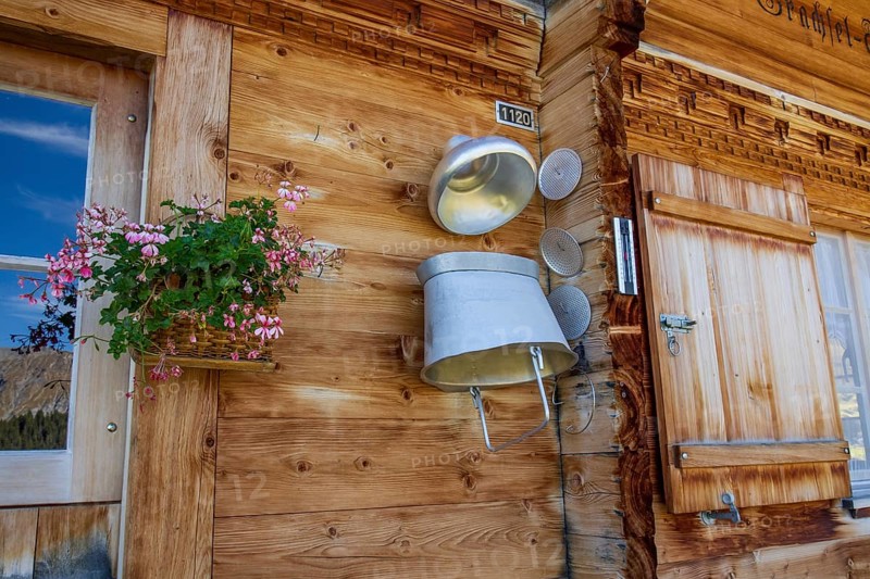 A rustic wooden wall with a window, a flower box and a decorative milk churn, typical alpine architecture, saas fee, graubünden, switzerland