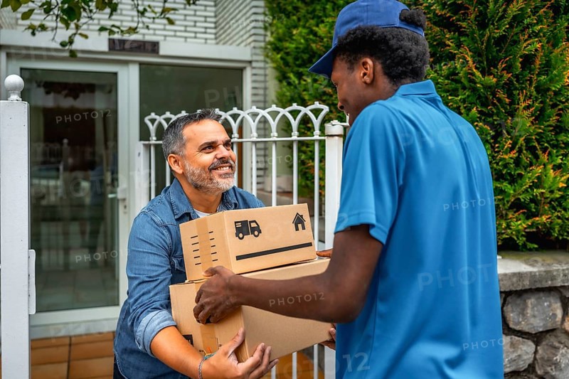 African delivery man giving packages to a costumer at home standing next to the entrance