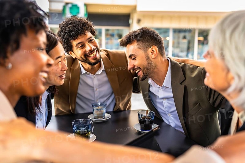 Multi-ethnic business team congratulating and celebrating embracing together sitting in a cafeteria