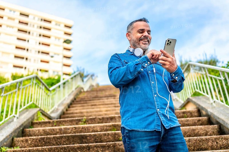 Low angle view photo of a mature man using phone and headphones standing on city stairs