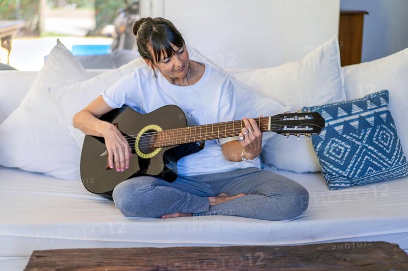 Adult woman playing the guitar while seated on her sofa at home