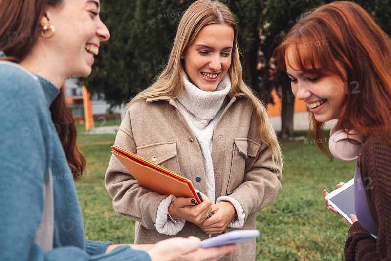 Group of three cheerful female collage students outside their dorm on a cold autumn day, walking on campus to get to their class