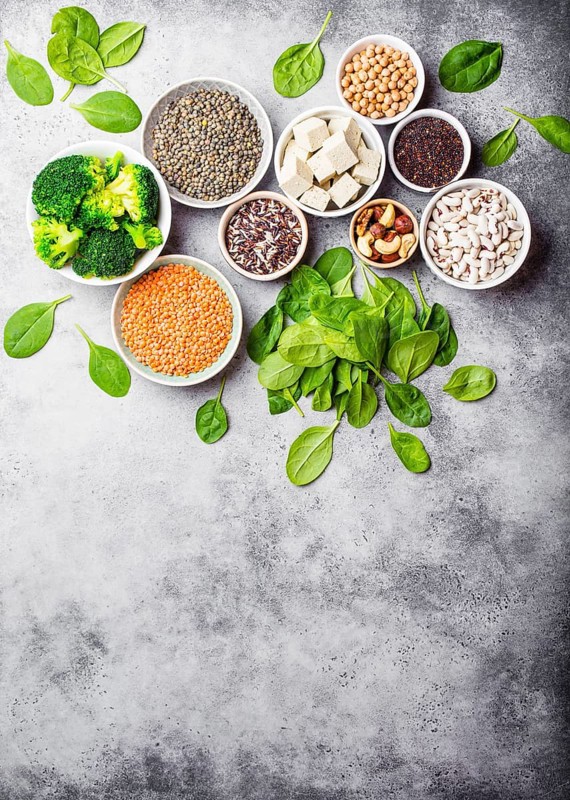Top view of different vegan protein sources with space for text: beans, lentils, quinoa, tofu, vegetables, nuts, chickpeas, rice, stone background. Healthy balanced vegetarian nutrition for vegans