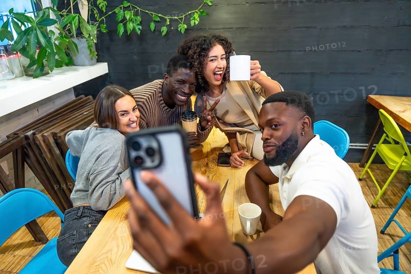 Diverse coworkers smiling taking selfie in the cafeteria of a modern coworking space