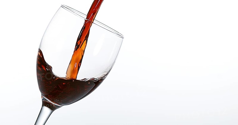 Red Wine being poured into Glass, against White Background