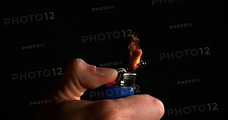 Lighter in Hand with Flame against Black background