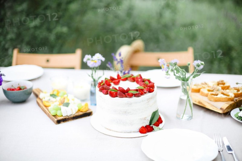 Tasty cake with berries placed on banquet table near flowers and dishware on summer day in garden