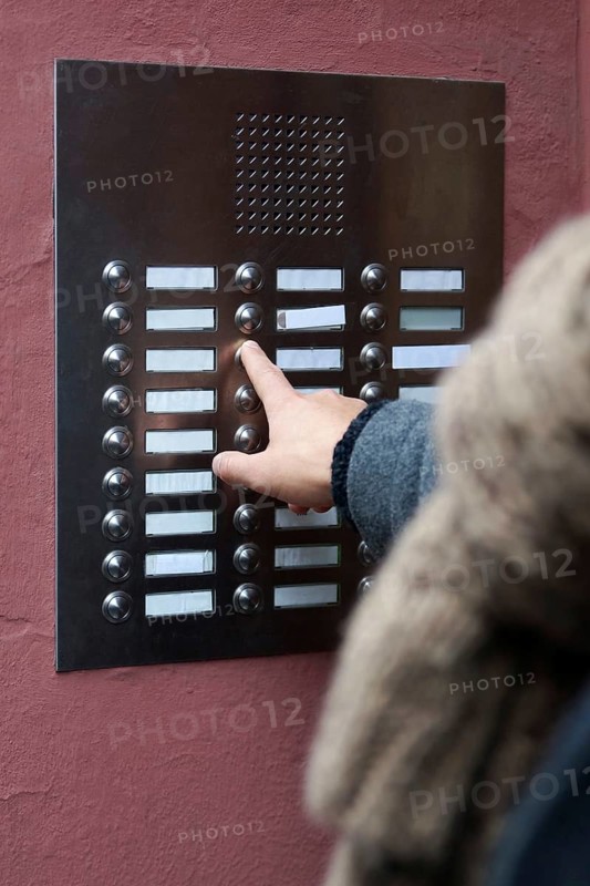 unrecognizable person ringing doorbell at apartment building. many blank nameplates