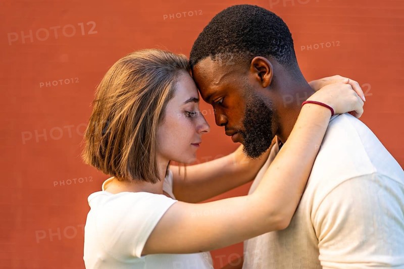 Close-up side view of multi-ethnic lovers embracing against red wall