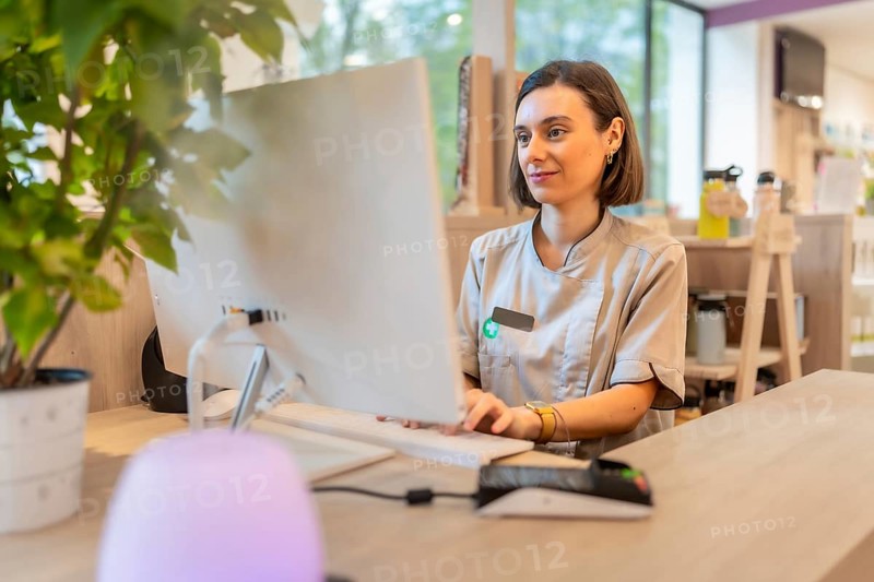 Young female pharmacist using computer sitting in the counter of a modern pharmacy store