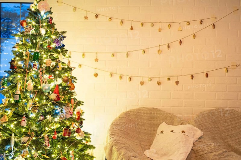 Christmas tree in white interior of a house with loft-style brick walls with garlands of glass toys on a rope. Glowing fairy lights decoration of the studio room. Cozy home in christmas and new year
