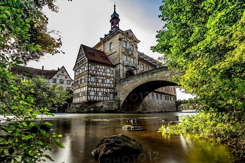Idyllic half-timbered house on a bridge over a river surrounded by lush greenery and clouds in the sky, old town hall Bamberg Bamberg