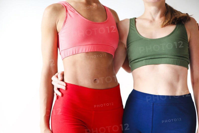 Two joyful happy women in sportive pink hoodie taking break after yoga classes or workout, standing against white wall in gym with copy space for text. Sport and healthy lifestyle