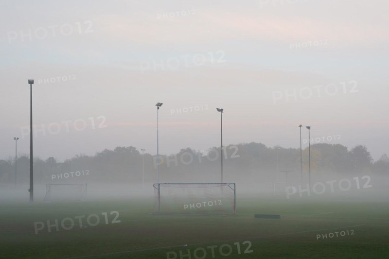 Empty and deserted soccer field in suburban area with goals and flood light poles on grey overcast day with fog and mist