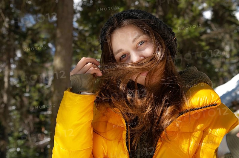 Happy young caucasian woman in a winter down jacket hat and mittens with happiness rejoices spreading her hands in a winter coniferous forest