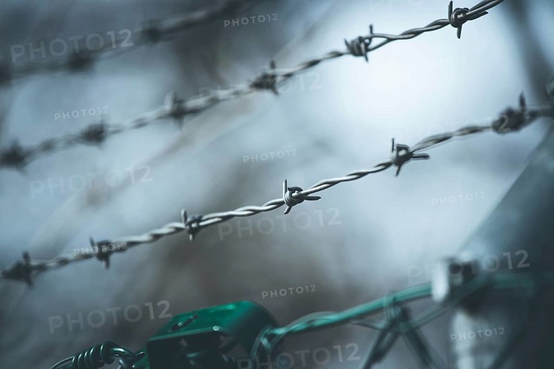 Barbed wire on a metal fence to demarcate the border, closeup, blurry background