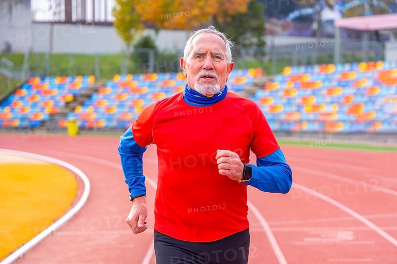 Frontal view portrait of an old man doing en effort running in an athletic track