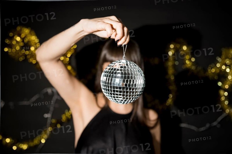 Young woman holding little disco ball near tinsel