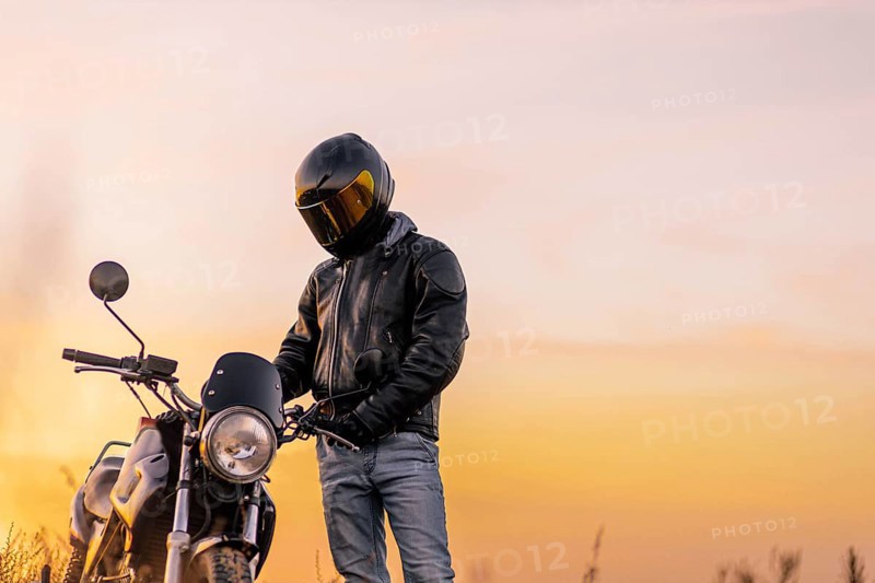 Motorcyclist in a helmet and motorcycle clothing stands at an old cafe racer