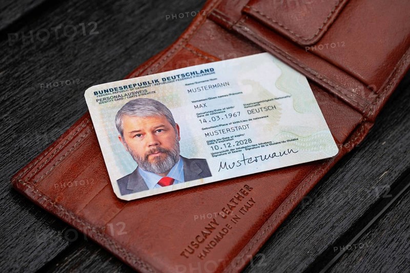 Identity card of the Federal Republic of Germany with a businessman around 50 years old lies on a brown leather wallet, labelled Tuscany Leather