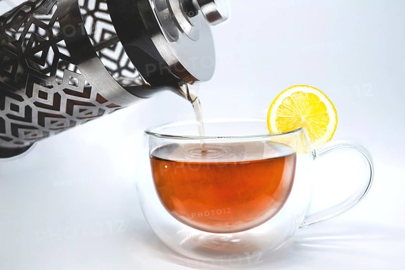 Glass teapot pouring black tea into cup isolated on the white