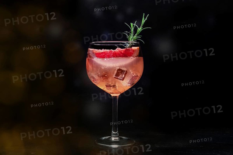 Fancy cocktail with fresh fruit. Gin and tonic drink with ice at a party, on a black background. Alcohol with pink grapefuit and rosemary, toned image, Food photography