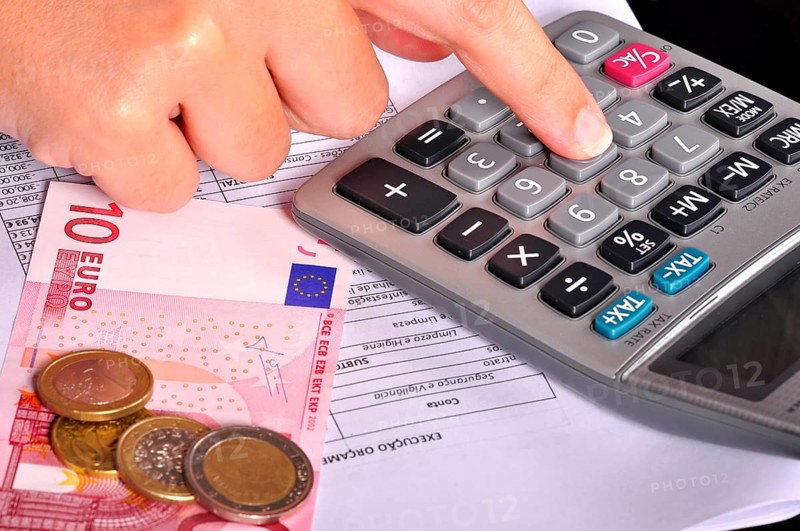 Business person doing accounts using a calculator with some money on the side