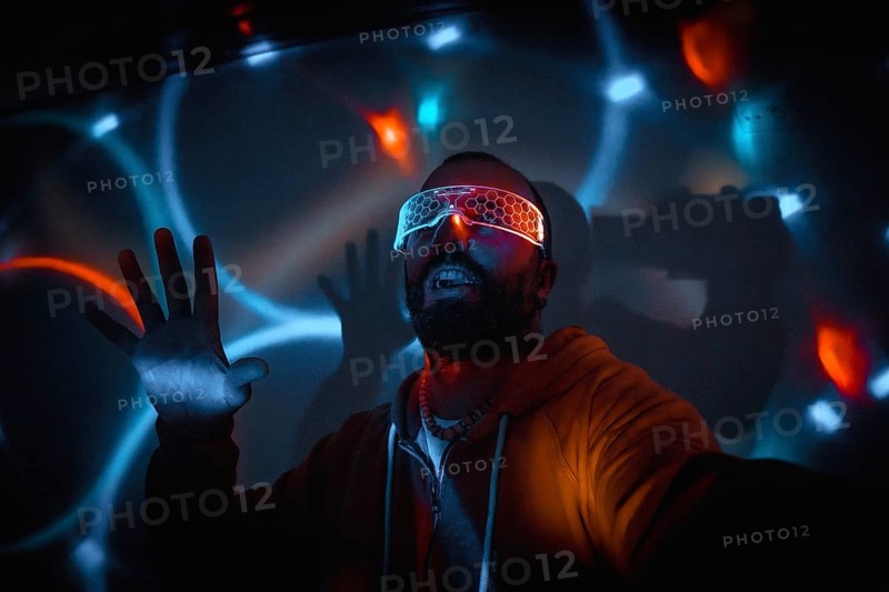 Bearded man wearing futuristic glasses interacting with virtual reality, moving hands and expressing excitement in dark room with colorful neon lights