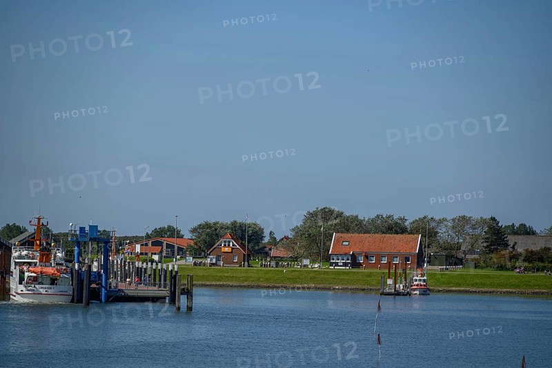 Small boats and traditional buildings at the harbour with calm water and blue sky, langeoog, east frisia, germany