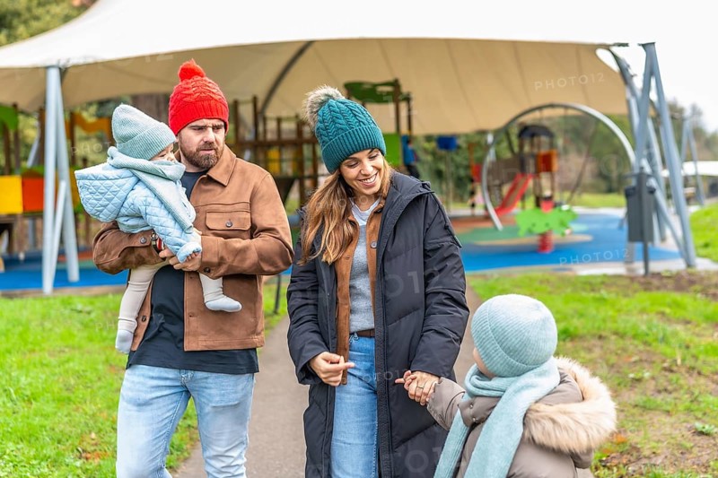 Happy family enjoying a winter day at the playground, bundled up in warm clothes and colorful hats, sharing smiles and laughter together