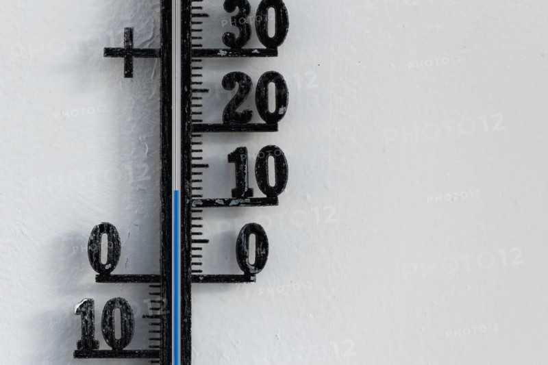 Classic analog thermometer hanging on white wall displaying warmth of twelve degrees celsius