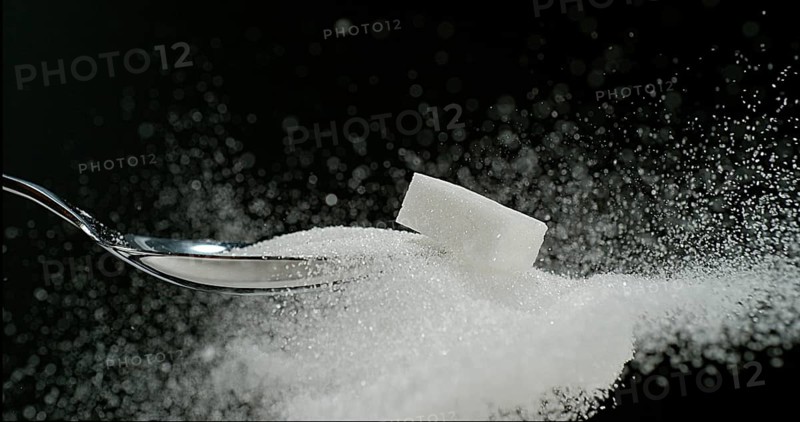 White Sugar Cube falling on Powder Sugar against Black Background
