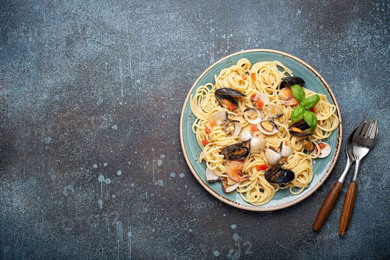 Italian seafood pasta spaghetti with mussels, shrimps, clams in tomato sauce with green basil on plate on rustic blue concrete background overhead. Mediterranean cuisine, space for text, food photography, food photography