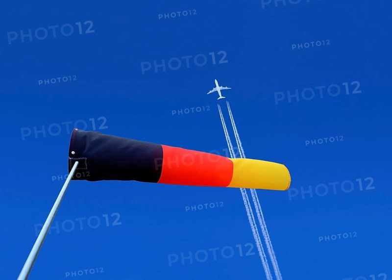 A passenger plane with vapour trails high in the blue sky and a german windsock