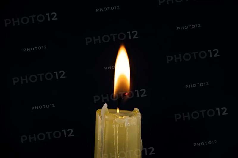 Burning yellow wax candle contrasting with the dark background, candle's gentle flame suggesting of remembrance, reflection and hope