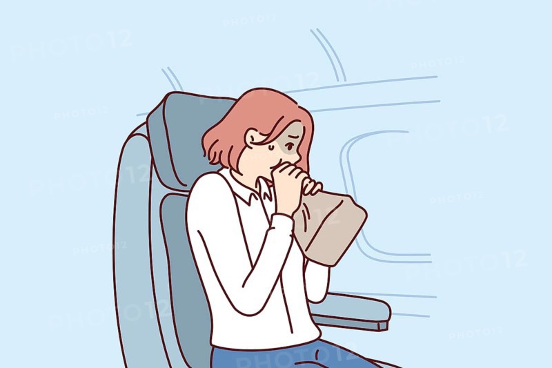 Woman passenger of airplane suffers from aerophobia and breathes into paper bag, sitting in airliner near porthole. Girl client of airline is stressed due to aerophobia or getting into turbulence zone