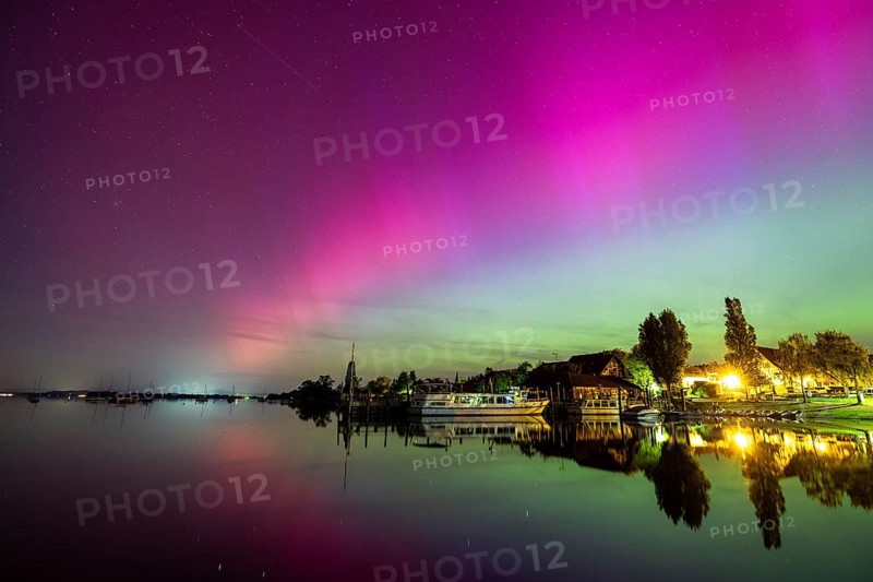Calm lake with vivid auroras reflected next to illuminated buildings, harbour, Allensbach, Lake Constance, Baden-Württemberg, Germany, Europe