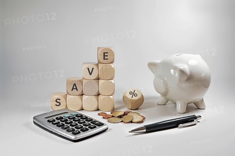 Home finance concept during inflation, wooden cubes with the word save and a percent sign, piggy bank, calculator and some coins on a grey beige background, copy space, selected focus