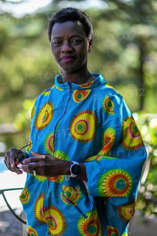 Young adult afro hair diverse model in traditional attire smiles softly while holding sunglasses outdoors