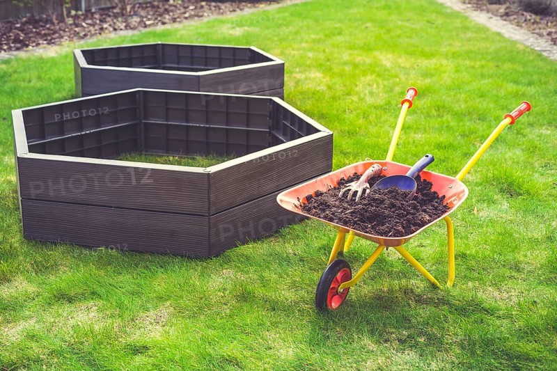 Garden barrow with soil and empty raised beds on grass prepared for filling with soil. Urban gardening concept