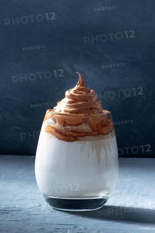 Dalgona cold coffee in a glass on a dark blue background with copy space. Trendy Korean milk shake