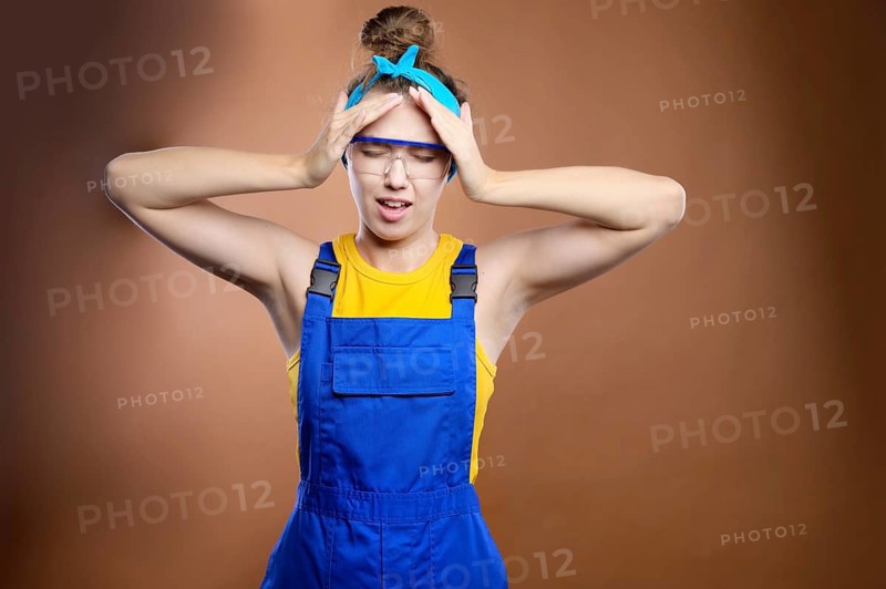Young attractive caucasian woman repairman construction worker in the uniform of a handyman holds her head with her hands from a headache in despair and stress because of worries during the repair. hands on the head