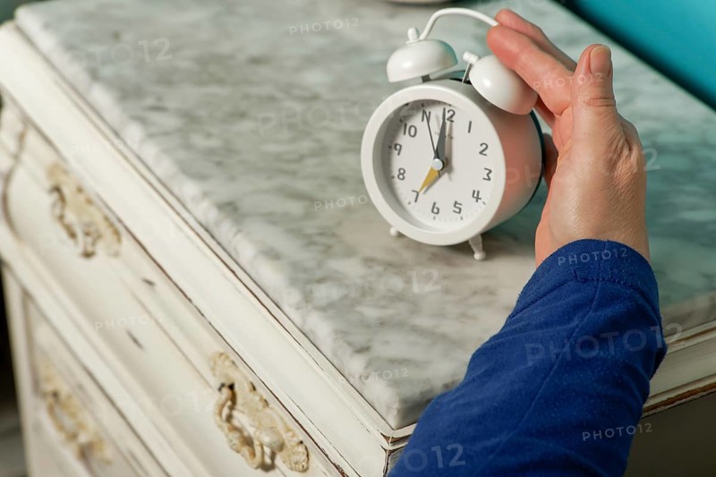 Woman in bed puts out her arm to turn off the alarm clock in the morning
