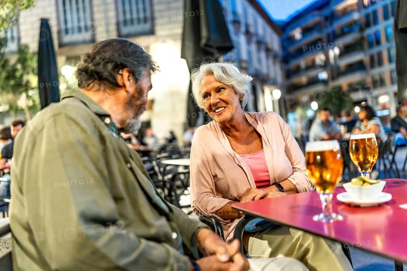 Senior male and female friends chatting enjoying beer in the city sitting on sidewalk bar