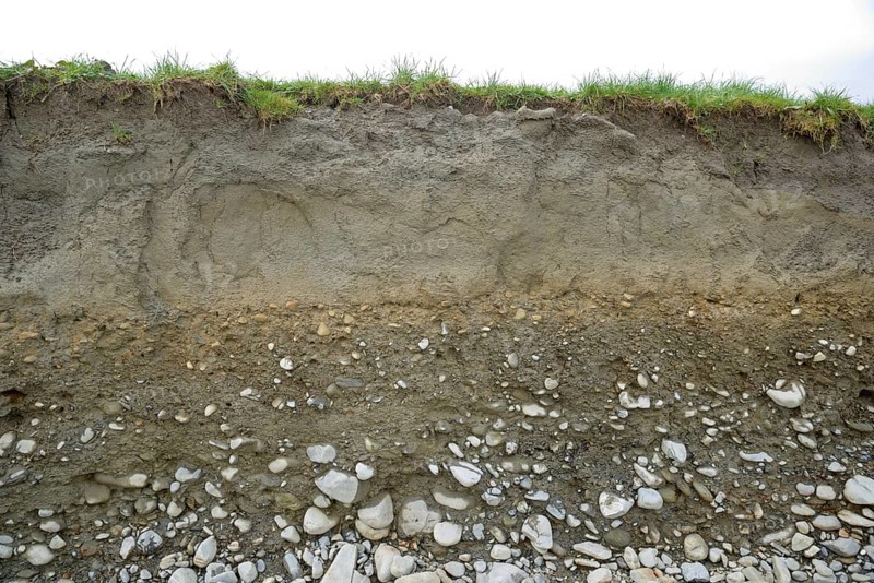 A cutting shows layers of topsoil, sub soil and shingle in typical West Coast farmland, South Island, New Zealand, Oceania