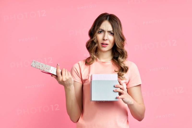 Young woman disappointed with her gift box on pink background. Bad present, emotion concept