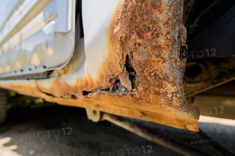 Body repair and welding work required. Rust on a gray old car. Rust hole on an old worn out painted metal surface